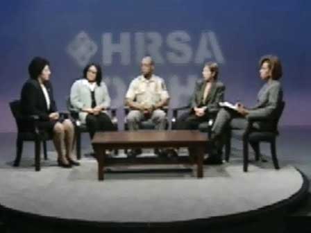Five individuals seated on stage look towards woman on left who is speaking.