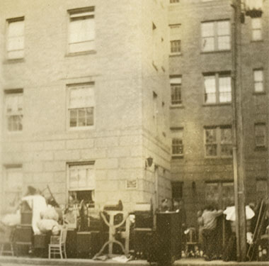 City street showing furniture and belongings on a sidewalk outside an apartment building.