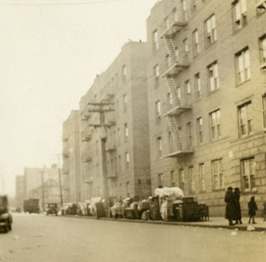 Street scape with furniture and belongings on a sidewalk outside a five-story apartment building.